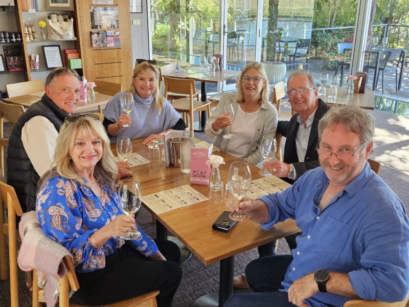 Group enjoying a wine tasting at a Coonawarra cellar door, seated with glasses and produce.