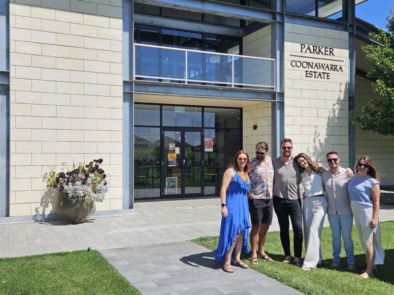 Group of seven visitors smiling in front of Parker Coonawarra Estate cellar door building.