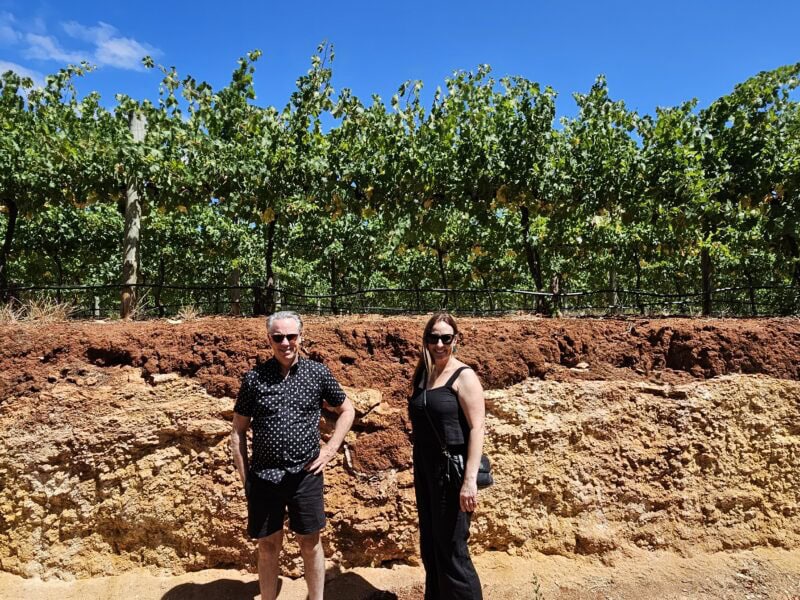 Two visitors standing in front of a cutaway profile of Terra Rossa soil beneath a Coonawarra vineyard.