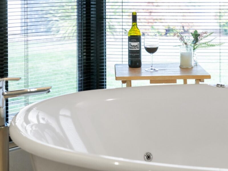 Coonawarra Experiences – Freestanding bath with wine, glass, and candle by window.