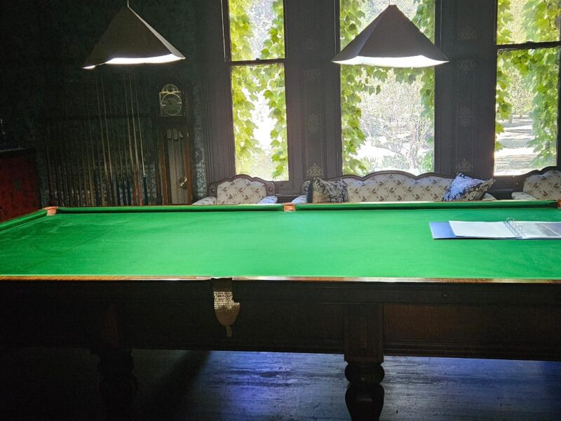 A vintage snooker table in a dimly lit room with large windows at Yallum Park.