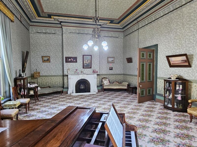 A parlour room with Victorian-era furniture, a piano, and intricate wallpaper at Yallum Park.