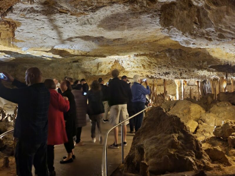 A group of tourists walking through Naracoorte Caves, observing the rock formations and taking photos.