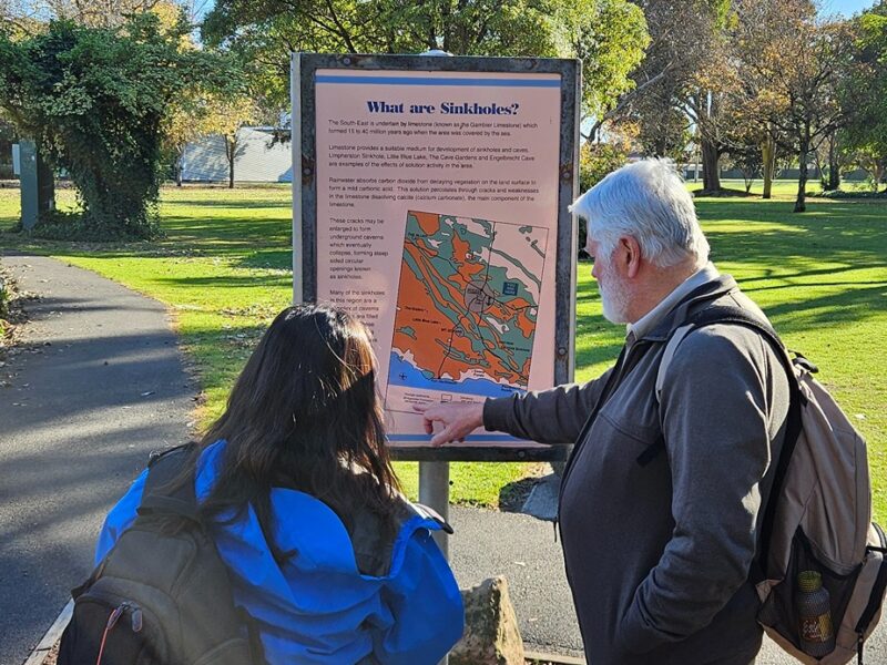 Two people reading a sign about sinkholes