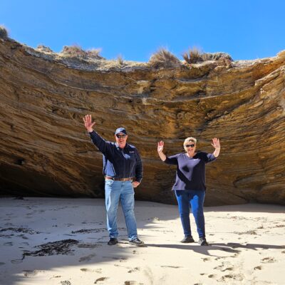 Two visitors posing under a dramatic rock formation on the Limestone Coast, celebrating nature’s wonders with joy