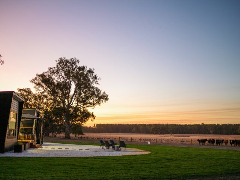 Stylish eco-accommodation at dusk with an outdoor deck and firepit overlooking a tranquil rural sunset.
