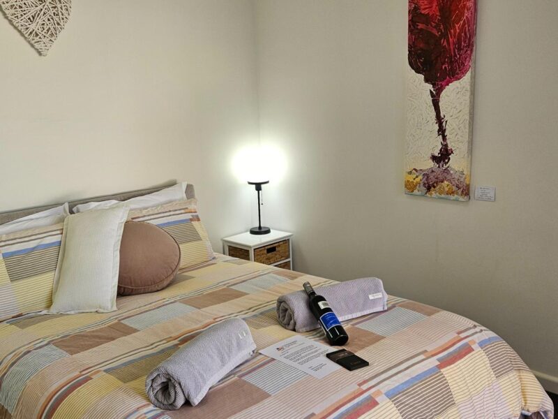 Coonawarra Experiences cosy bedroom with queen bed, wine, towels, and French doors opening to garden.