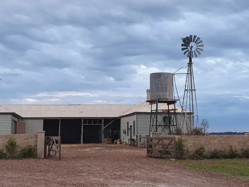 Historic stables, water tank and windmill with the gate open, under a heavy grey cloud cover at Yallum Park