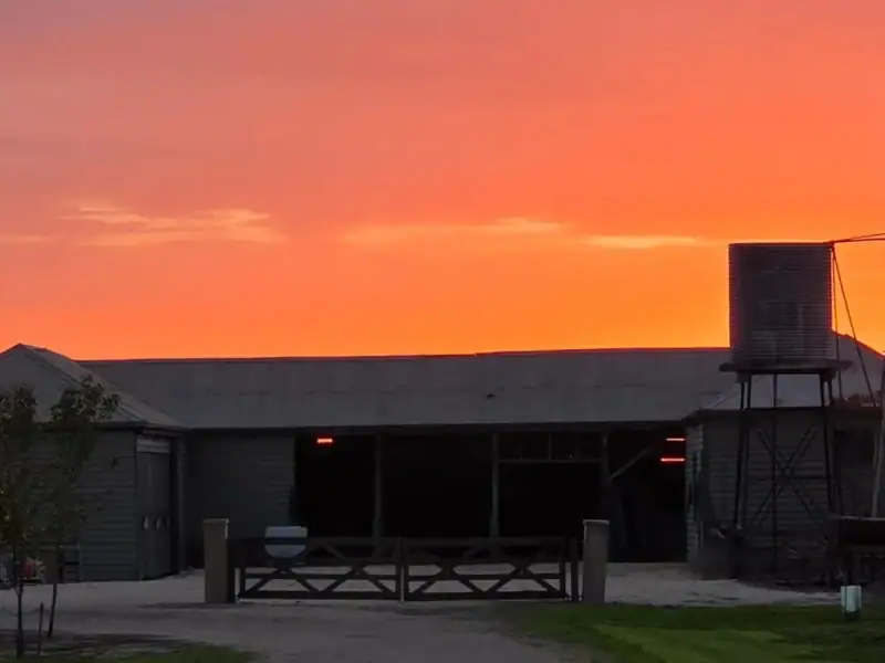 Silhouette of a historic stables, water tank and windmill against a vivid orange and pink sunset sky at Yallum Park, Penola