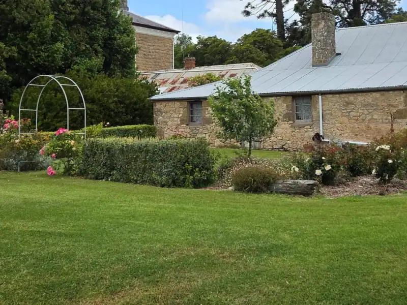 Stone outbuilding with corrugated iron roof and chimney beside a rose garden and arched trellis at Yallum Park