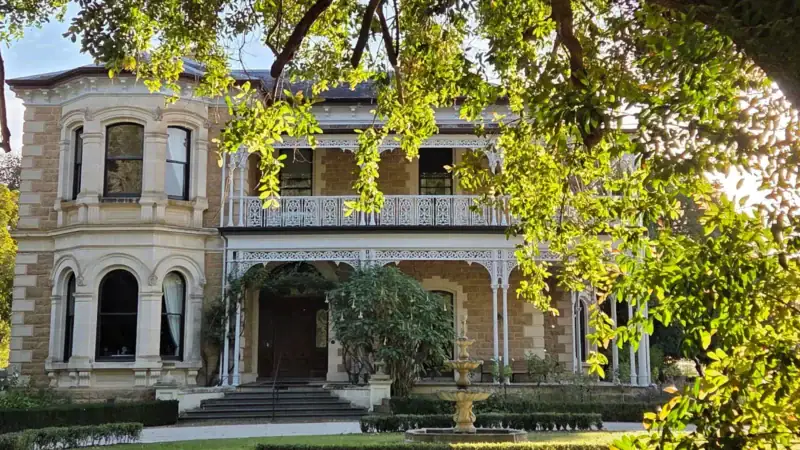 Yallum Park's sandstone Victorian mansion facade and veranda framed by overhanging tree branches, Penola South Australia